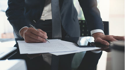 A man signs paperwork at a desk